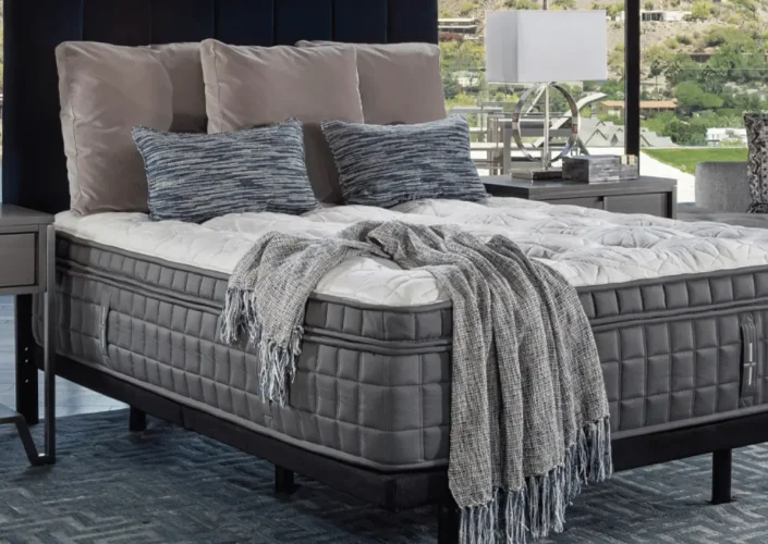 King Koil Huntington Tight Top Plush mattress displayed with decorative pillows and a cozy throw blanket in a modern bedroom setting, emphasizing comfort and luxury for enhanced sleep quality.